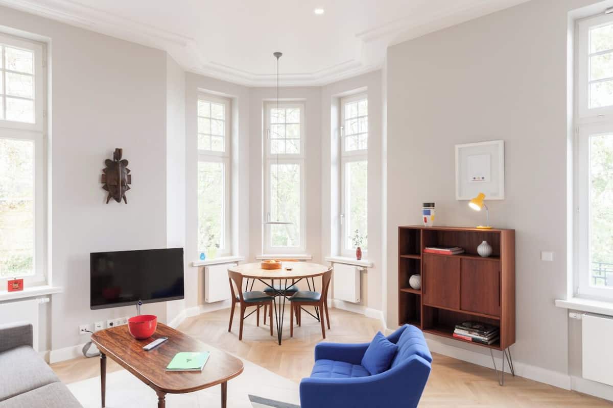 A modern living room with a television, dining table, blue sofa, and a wooden bookshelf.