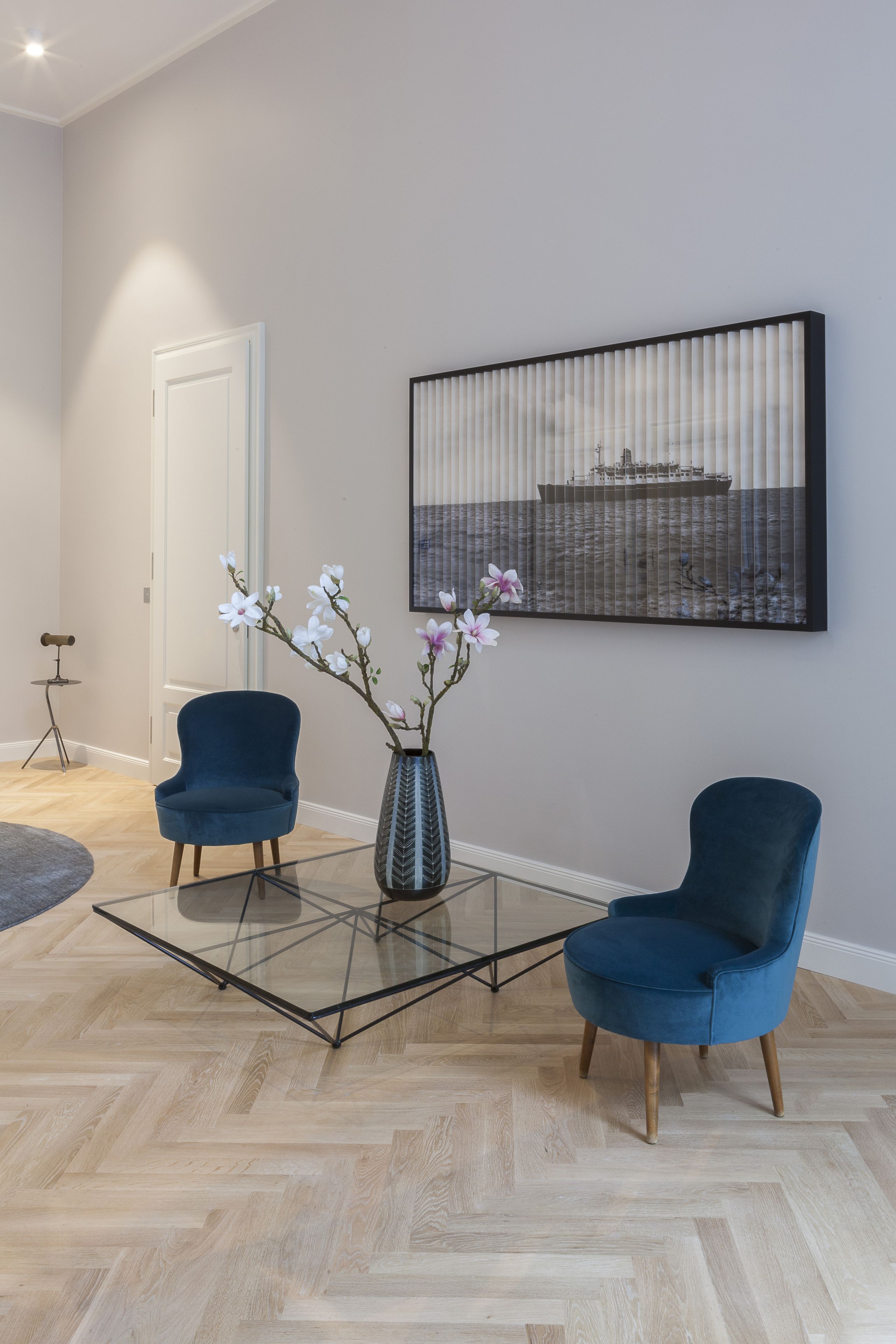 Un salon moderne avec deux fauteuils bleus, une table basse en verre et un vase rempli de fleurs.