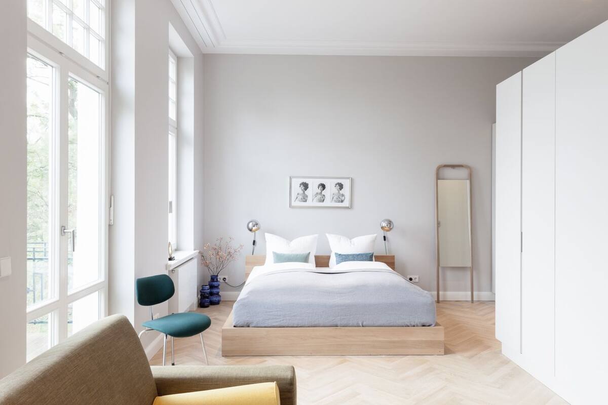 A modern bedroom with a large bed, a chair, a desk, and a mirror.