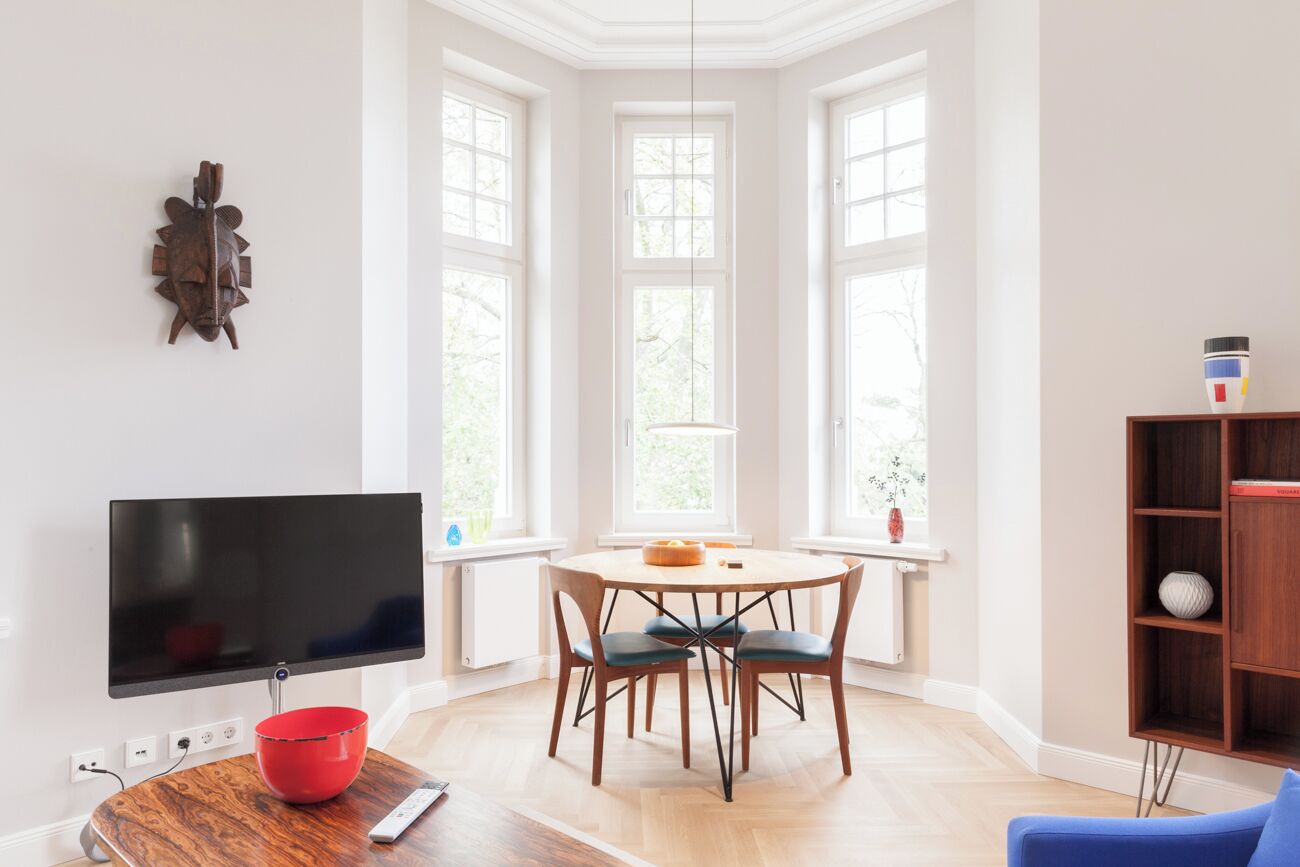 A modern living room with a flat-screen TV, a wooden dining table with chairs, a red bowl, and a blue sofa.