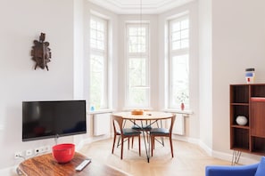 Moderni olohuone, jossa on litteänäyttöinen televisio, puinen ruokapöytä ja tuolit.