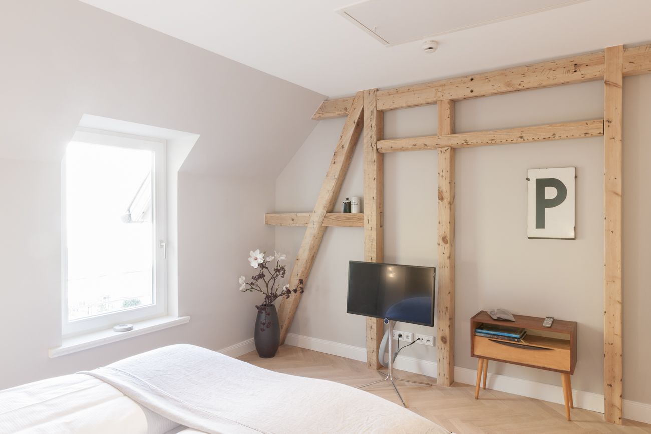 Une chambre à coucher avec un lit, un bureau et une chaise, une télévision, un vase avec des fleurs et une fenêtre.