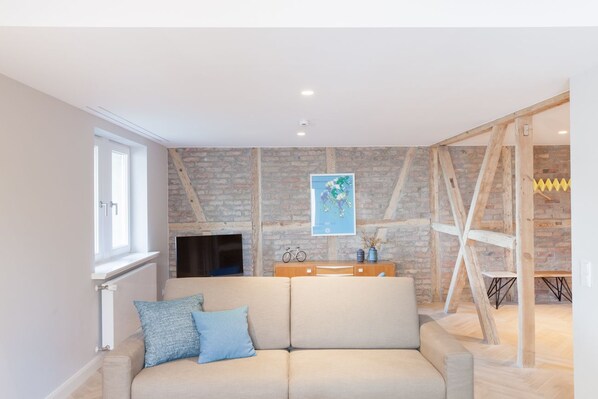 A modern living room with a beige sofa, a wooden coffee table, and a brick wall. - OSTKÜSTE - Villa Staudt Design Apartments (Heringsdorf)
