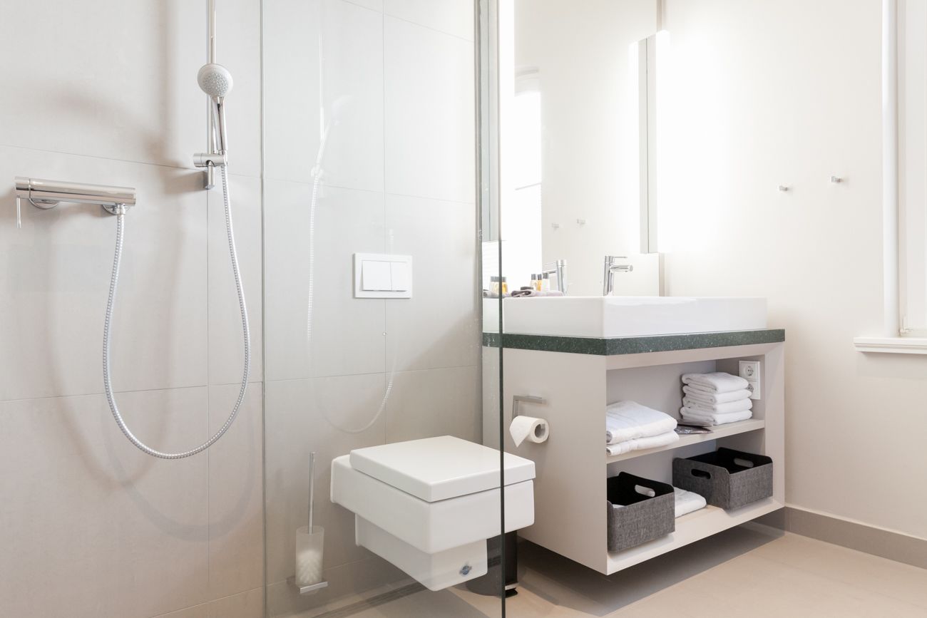 A modern bathroom with a glass shower enclosure, a white toilet, a sink with a green countertop, and storage shelves.