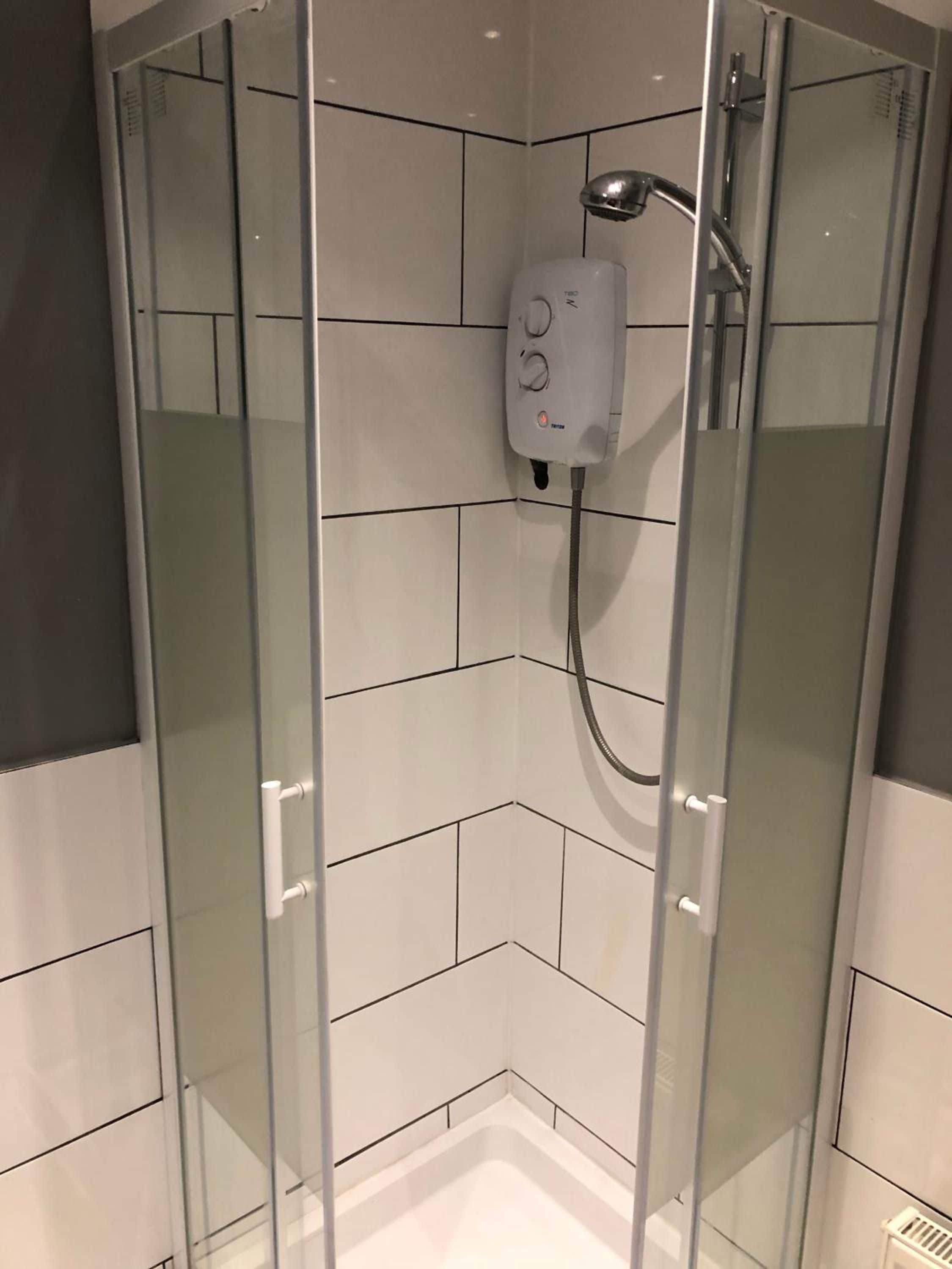 Et brusekabine med glasvægge, håndbruser og betjeningspanel.