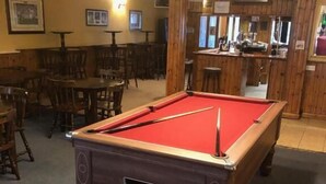 A pool table in a room with wooden walls and tables, a bar area, and framed pictures on the walls. - The Pheasant Inn (Dunstable)