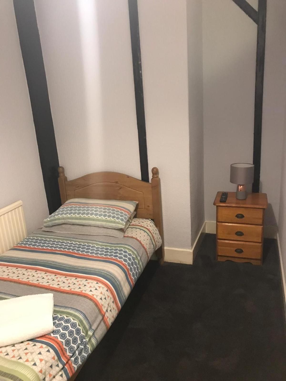 Una cama pequeña y bien hecha, con cabecera de madera y colcha a rayas coloridas.