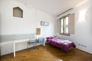 A bedroom with a bed, a desk, a chair, a window, and a wall-mounted light fixture. - Vigna Nuova (Florence)