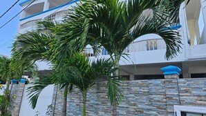 A multi-story building with a white exterior and blue accents, surrounded by palm trees and a stone wall. - LeBovallon B&B (Mahebourg)