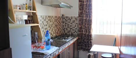Una cocina compacta con refrigerador, estufa y una pequeña mesa con un taburete.