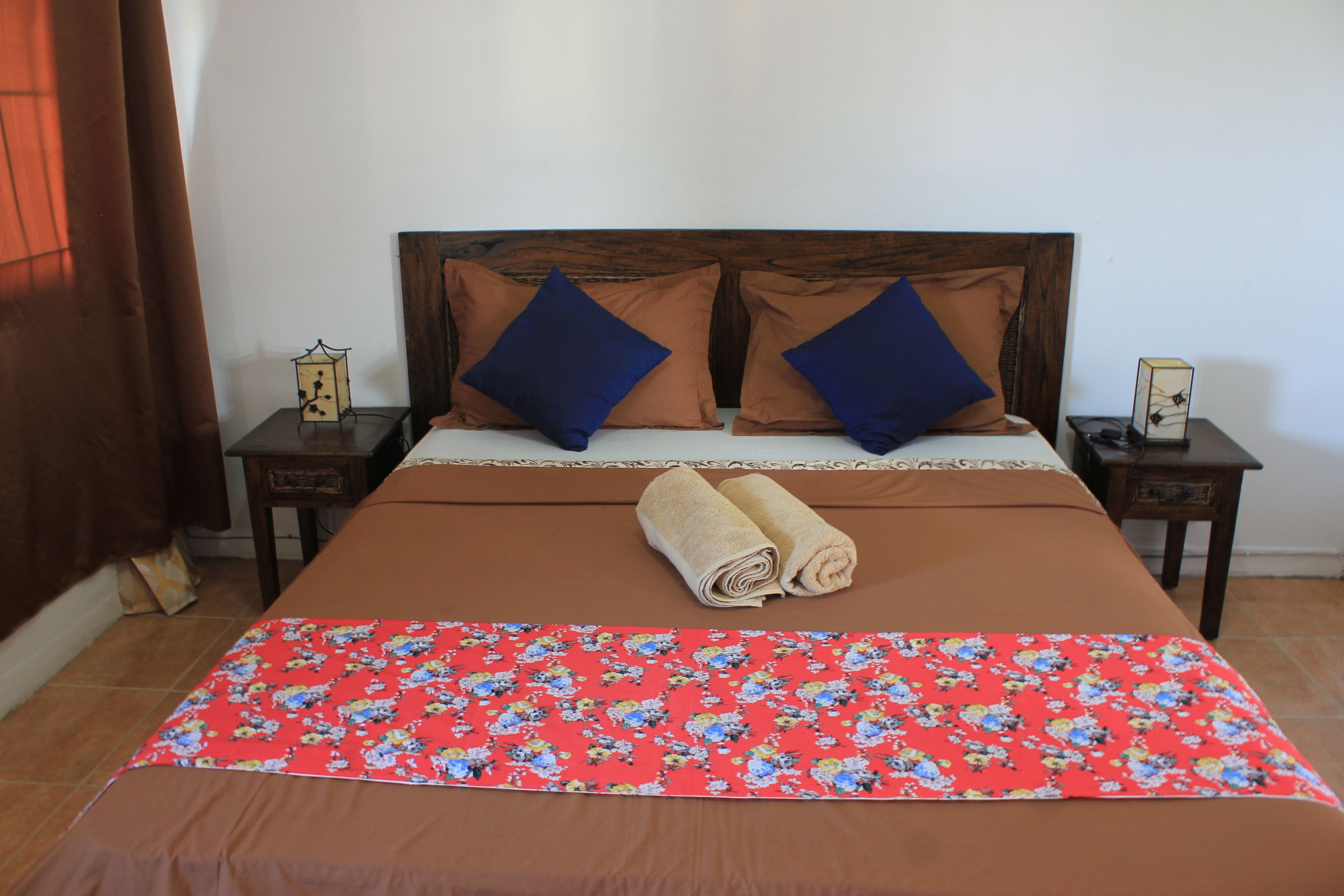 A neatly made bed with a floral bedspread, two pillows, and a rolled towel.