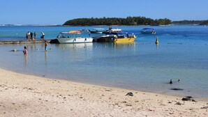 A beach with several boats docked near the shore, a sandy beach, and a forested island in the background. - LeBovallon B&B (Mahebourg)