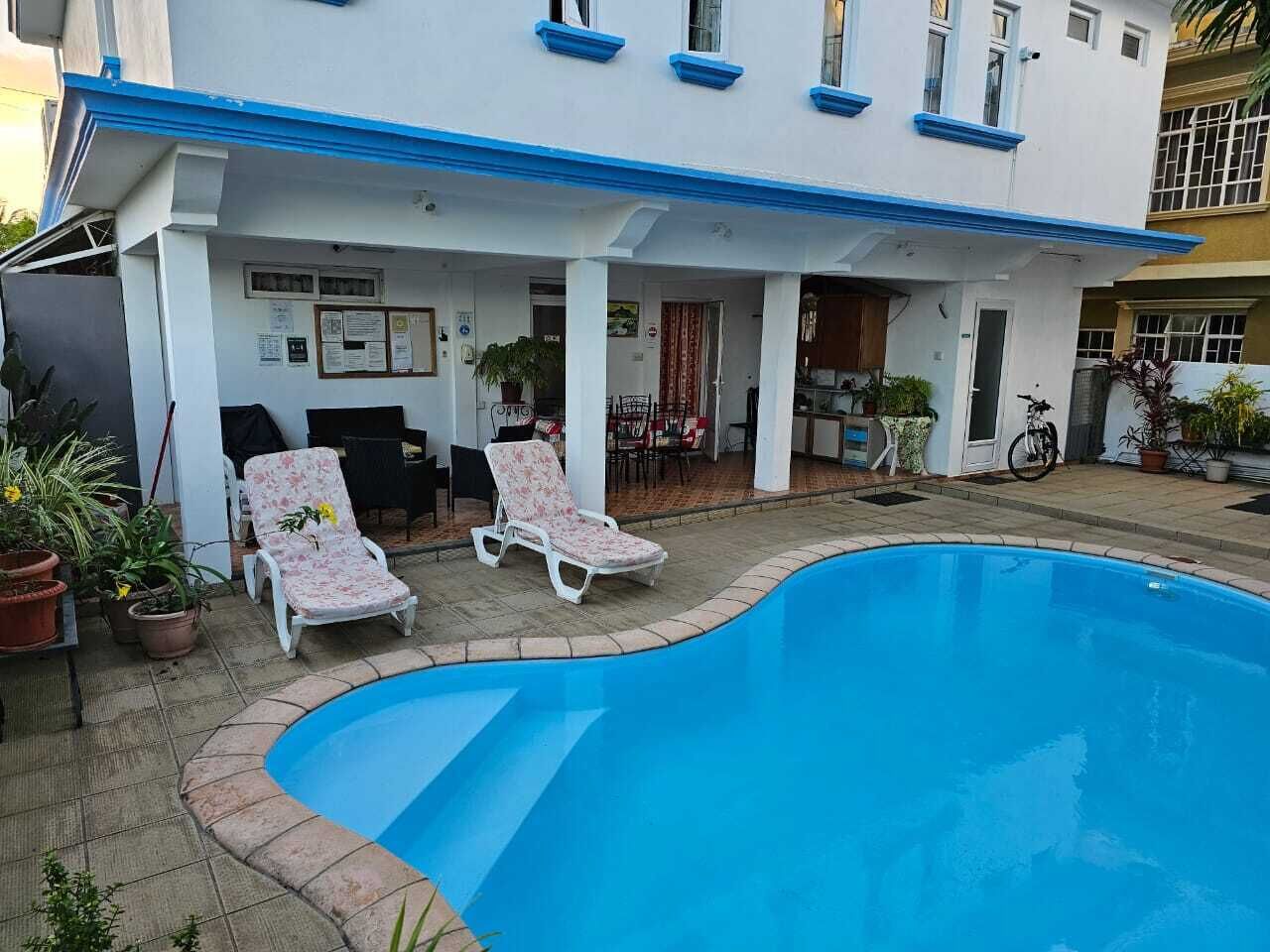 A pool area with two lounge chairs and a small patio with potted plants.