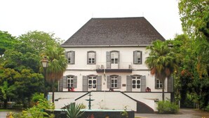 A two-story building with a symmetrical facade, large windows, and a central entrance with a staircase. - LeBovallon B&B (Mahebourg)
