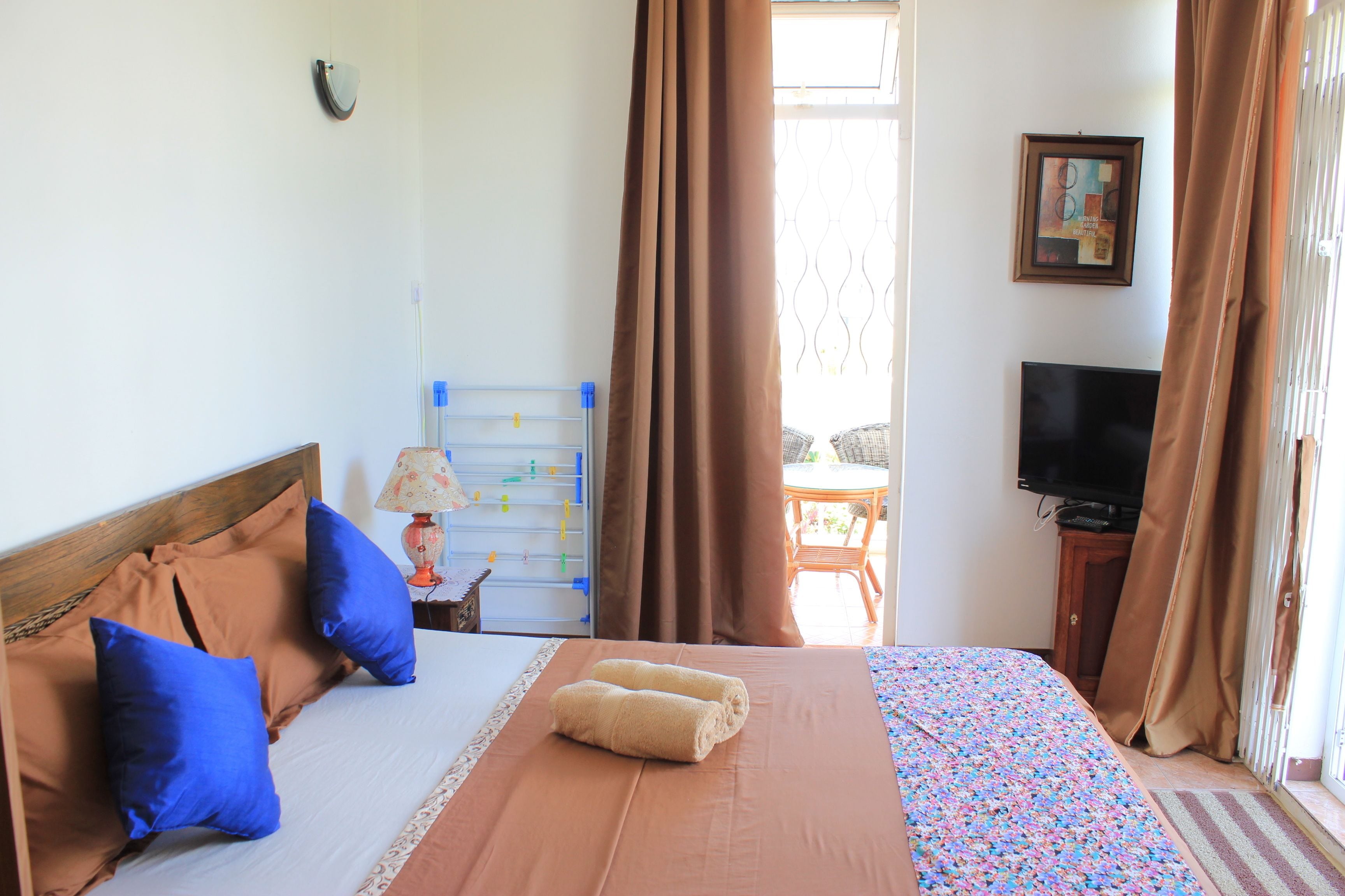 A hotel room with a bed, pillows, a TV, and a window with curtains.