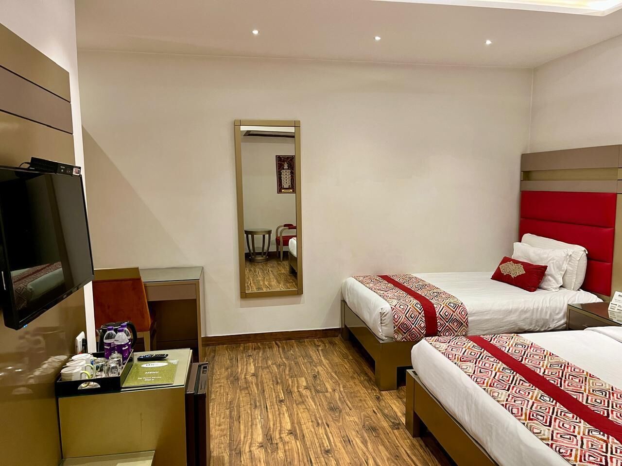 A hotel room with two beds, a TV, a desk with a chair, and a mirror.
