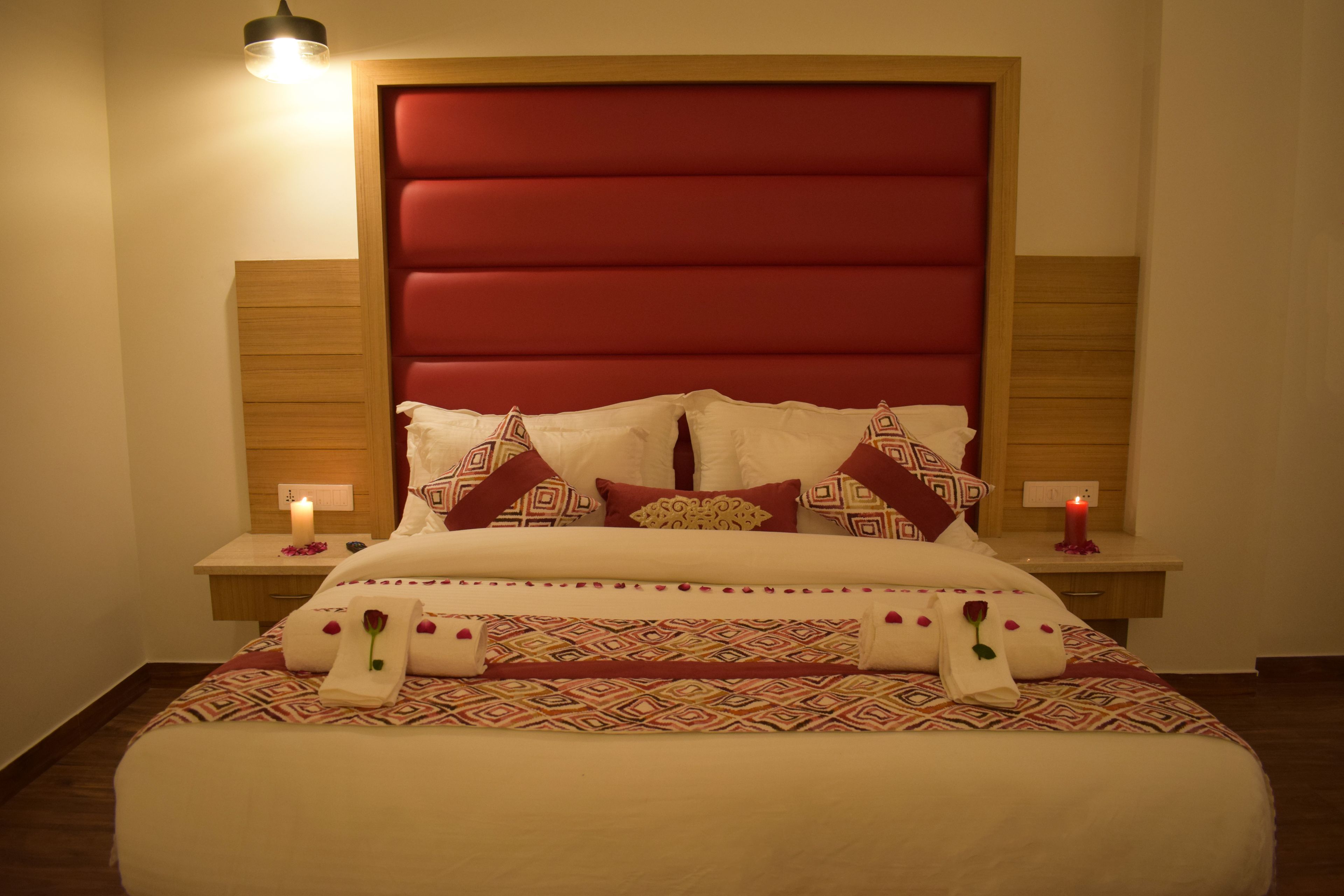 A neatly made bed with patterned bedding, two bedside tables with candles, and a red upholstered headboard.