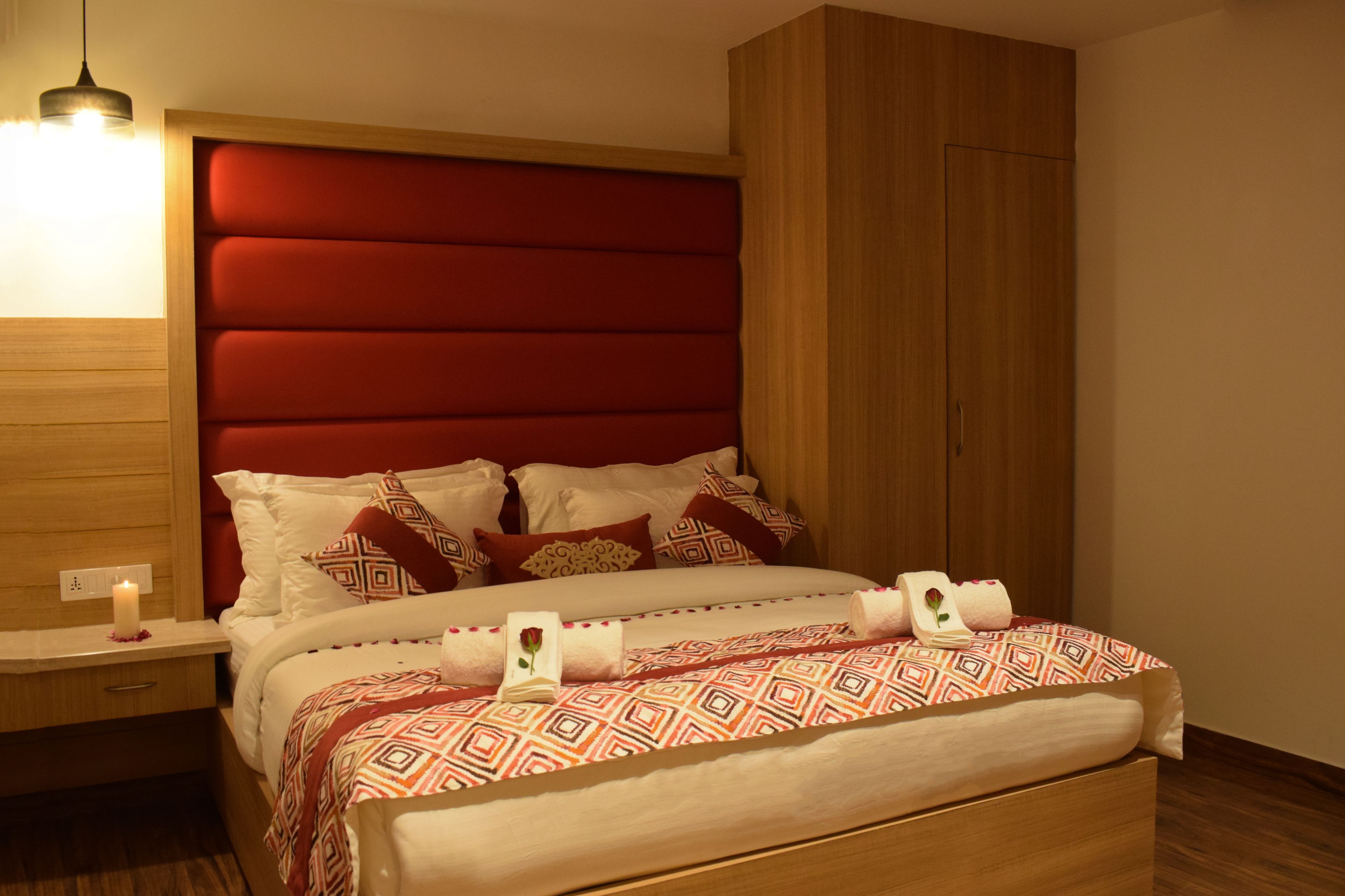 A neatly made bed with patterned bedding, a bedside table with a lamp, and a wooden wardrobe.