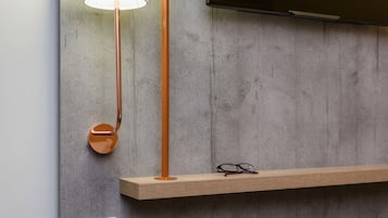 A modern room with a concrete wall, a mounted television, a wooden shelf with glasses, a floor lamp, and a power outlet.