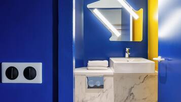 Een badkamer met een blauwe wand, een witte wastafel, een spiegel met verlichting en een gele accentwand.