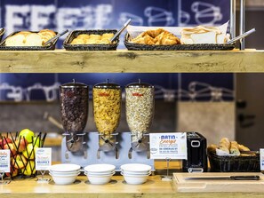 A breakfast buffet with cereal options, bread, and apples. - ibis budget Lyon Est Beynost (Beynost)