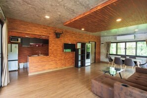 A spacious room with a wooden floor, a sofa, a dining table with chairs, and a kitchen area with a refrigerator, microwave, and sink. - Saree Lagoon Villa Koh Samui (Koh Samui)