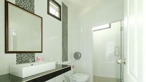 Une salle de bain avec un lavabo, des toilettes et une douche, le tout de couleur blanche.