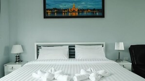 Une chambre d’hôtel avec un lit, deux tables de chevet, une chaise, un tableau au mur et une vue sur le paysage urbain.