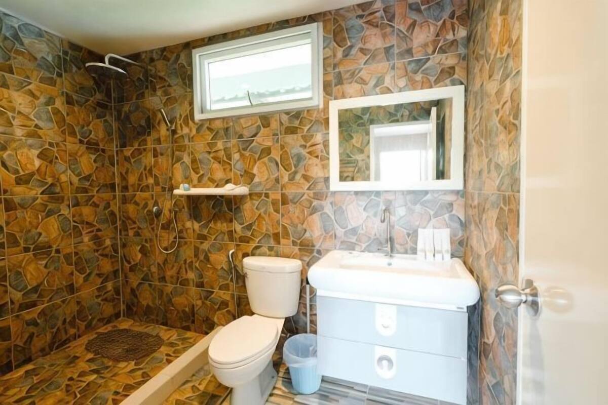A bathroom with a shower, toilet, sink, and a mirror.