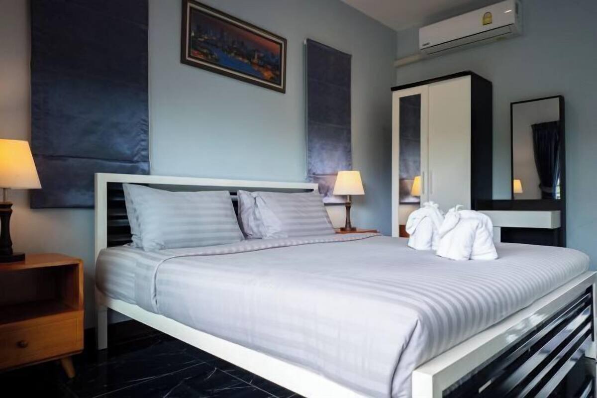 A neatly made bed with pillows, a nightstand with a lamp, a wardrobe, and a painting on the wall.