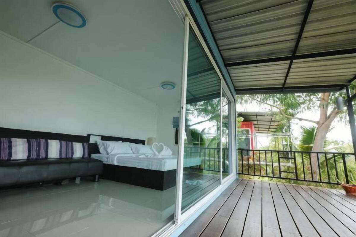 A modern room with a bed, a sofa, a glass door leading outside, and a balcony with a railing.
