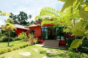 A modern house with a red exterior, a glass door entrance, and a well-maintained garden with various plants. - Saree Lagoon Villa Koh Samui (Koh Samui)