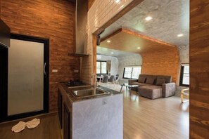 A modern kitchen with a central island, a dining area with a sofa and chairs, and a lofted living space with a fireplace. - Saree Lagoon Villa Koh Samui (Koh Samui)