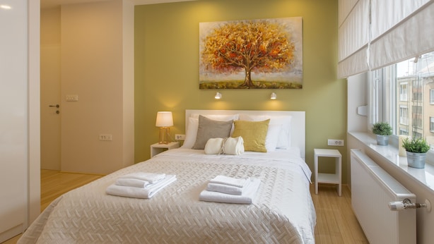 A neatly made bed with white linens and towels, a painting of a tree on the wall, and a window with potted plants. - MirÓ Studio apartments Zagreb (Zagreb)