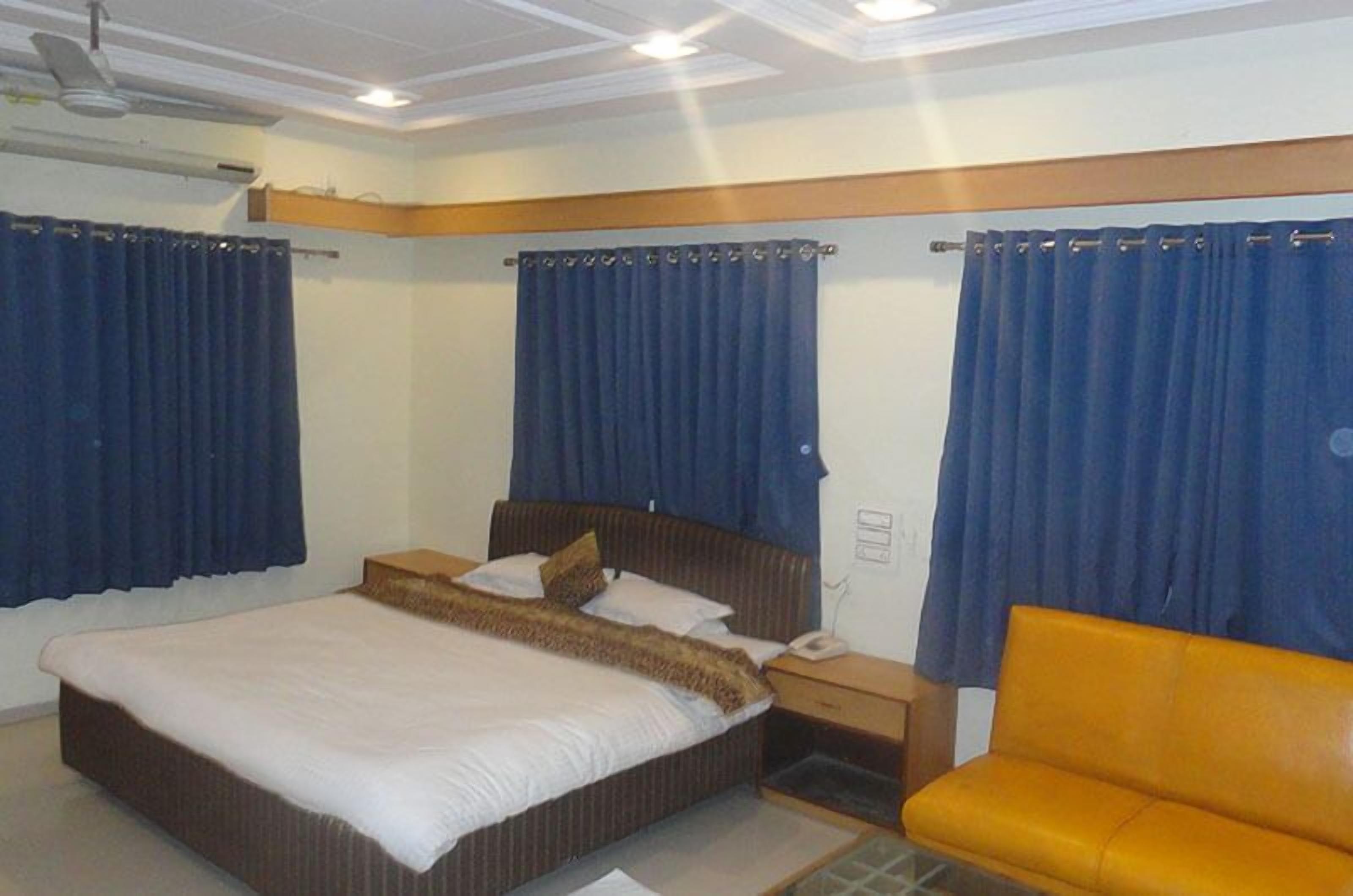 Una habitación de hotel con cama, mesita de noche, teléfono y una silla amarilla.