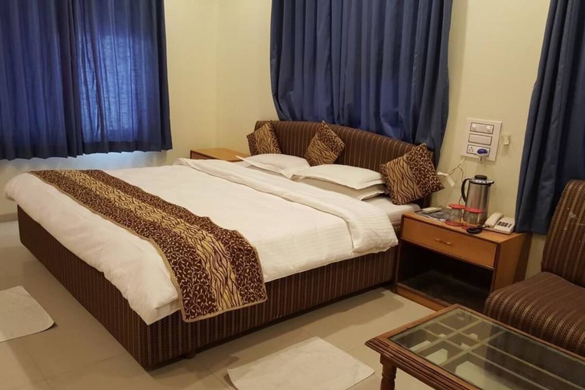 Una habitación de hotel con una cama, una mesita de noche, un fabricante de café, un teléfono y un área de descanso con una mesa de vidrio.