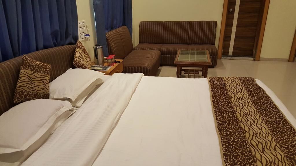 Hotellihuone, jossa on sänky, sohva, pieni pöytä ja kuviollinen päiväpeitto.