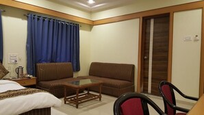 A hotel room with a bed, two striped sofas, a small wooden table, and a red chair. - Hotel Riviera Executive (Chhatrapati Sambhajinagar)