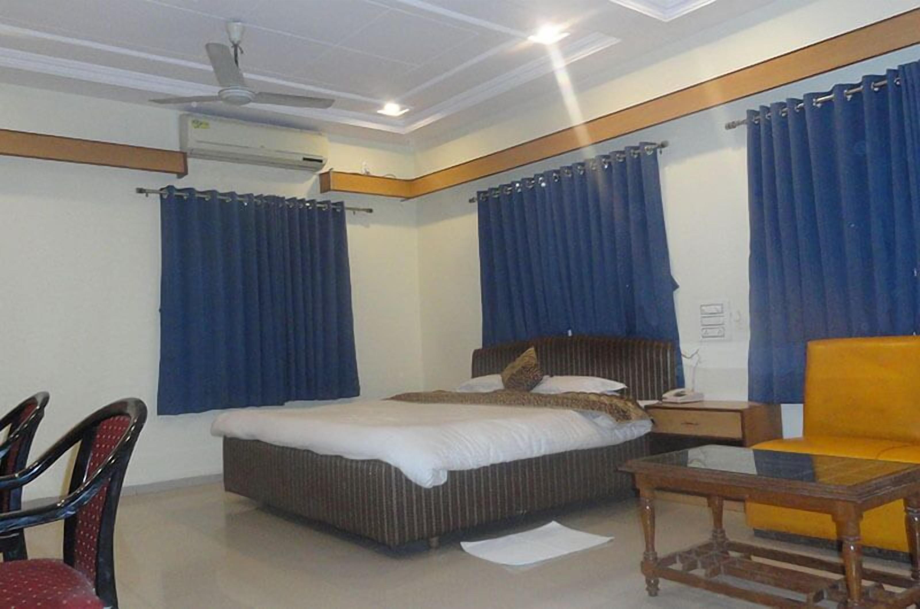 A hotel room with a bed, a chair, a small table, and a ceiling fan.