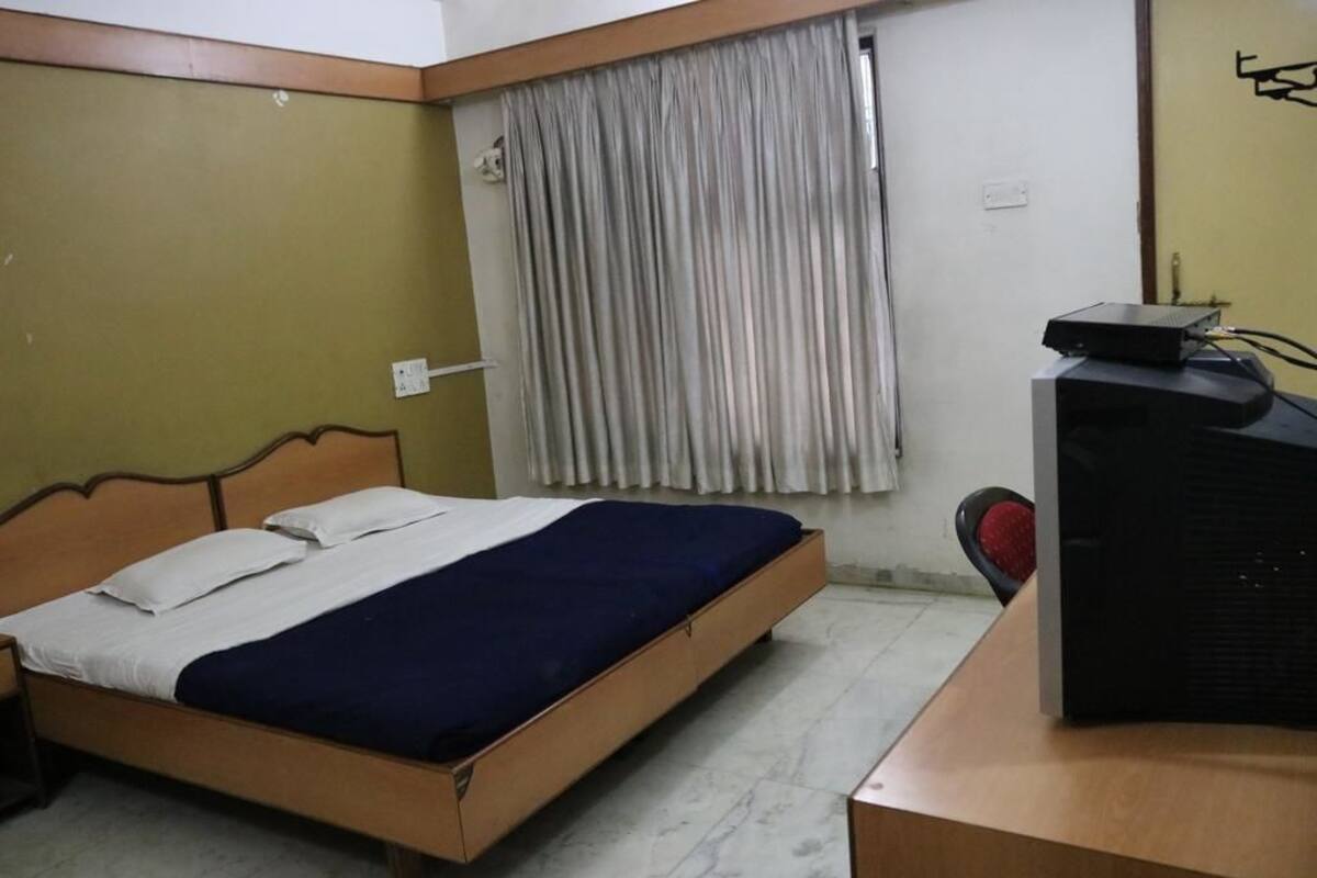 Una habitación con una cama, un escritorio con computadora, una ventana con cortinas y una estantería en la pared.