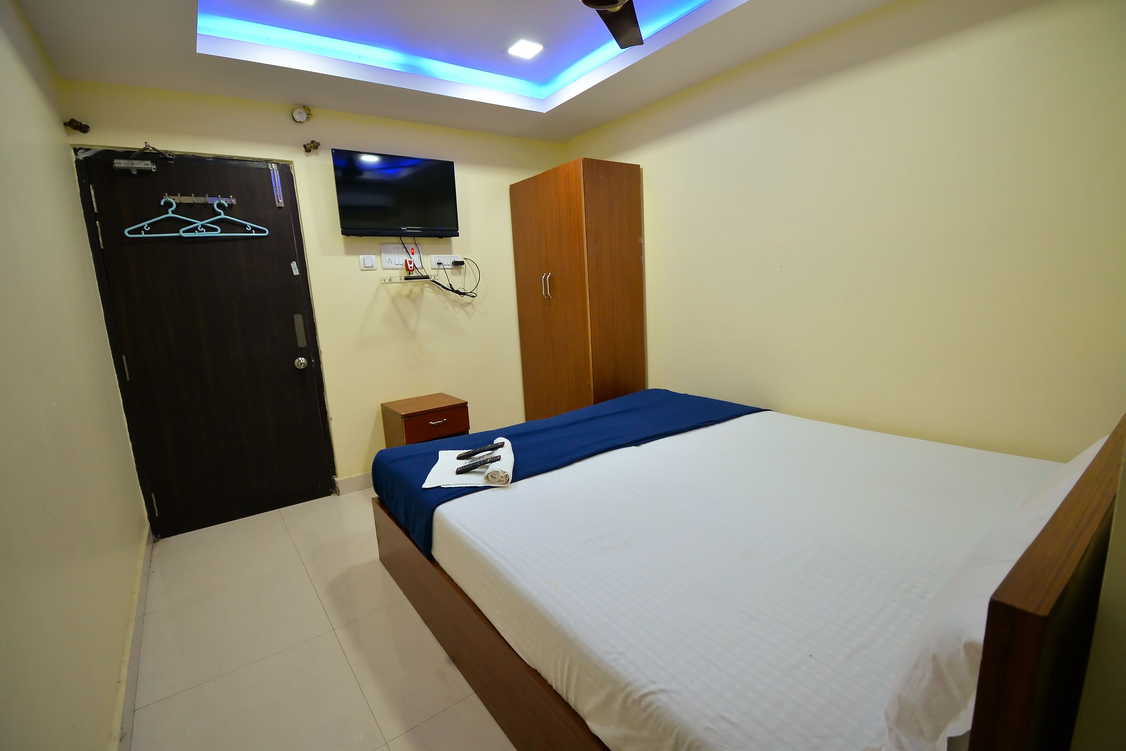 Habitación de hotel con una cama, un armario, un televisor montado en la pared y una puerta con un gráfico de perchero.