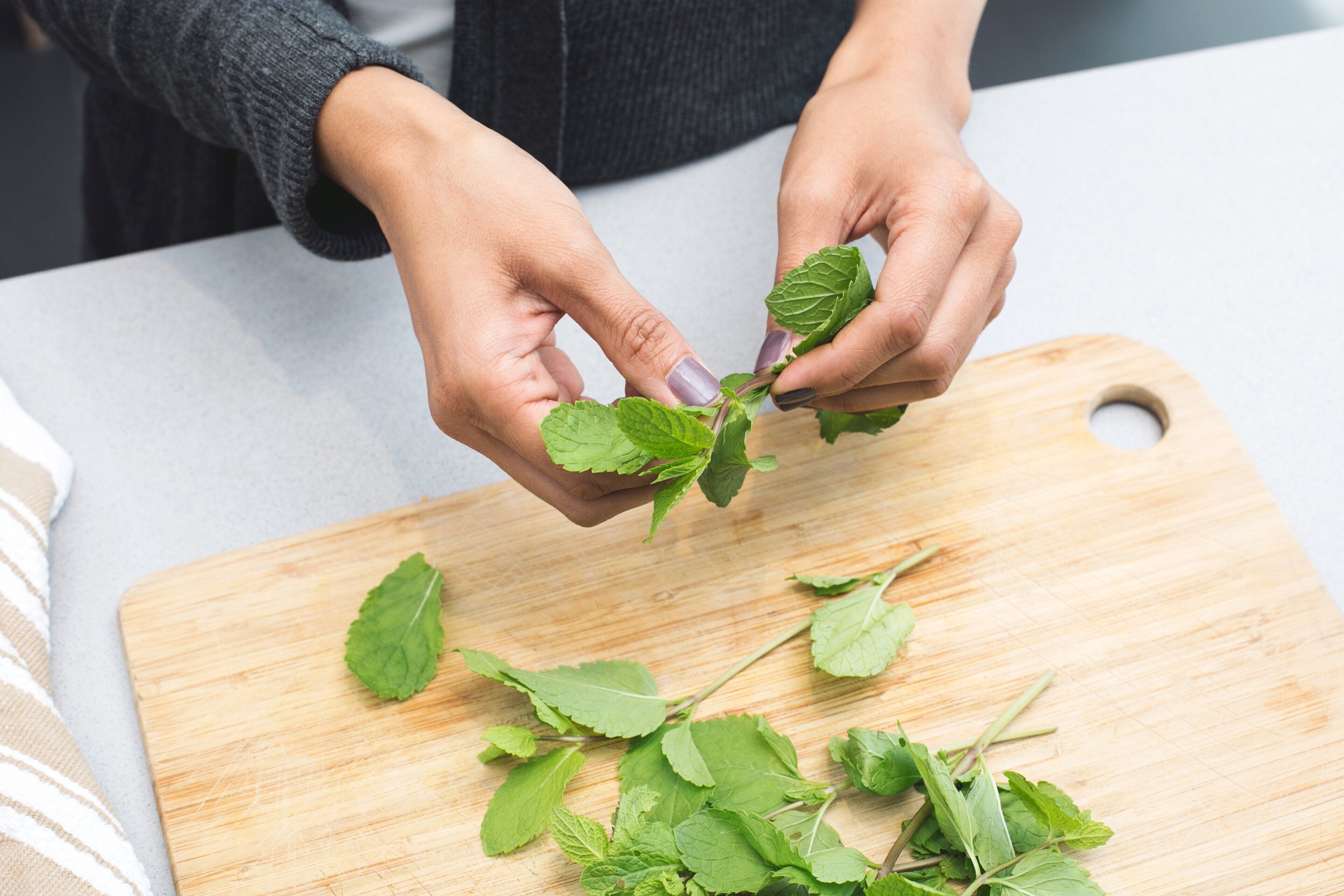 Hands holding fresh mint leaves on a wooden cutting board.