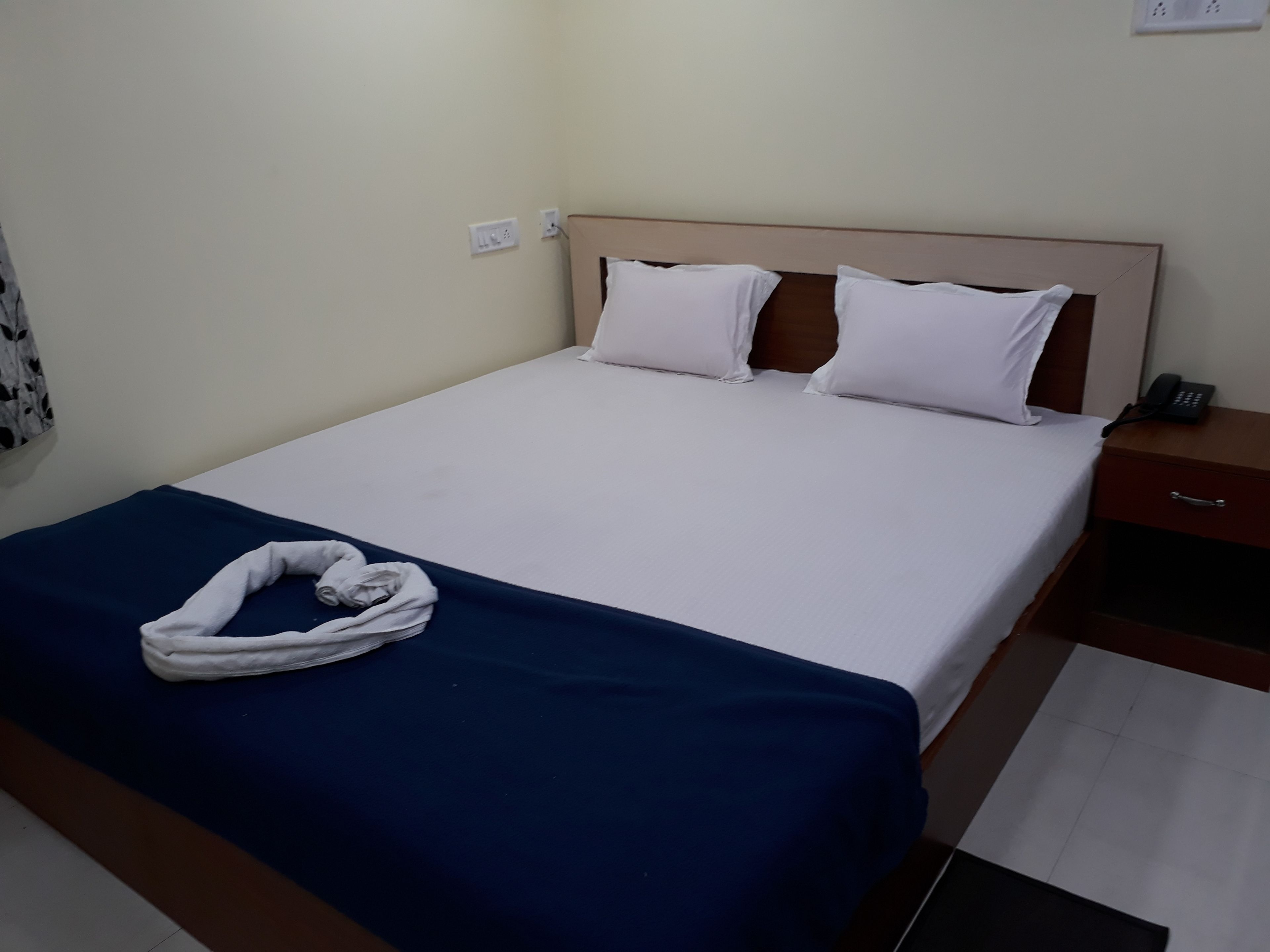 A hotel room with a bed, a bedside table with a phone, and a towel on the bed.