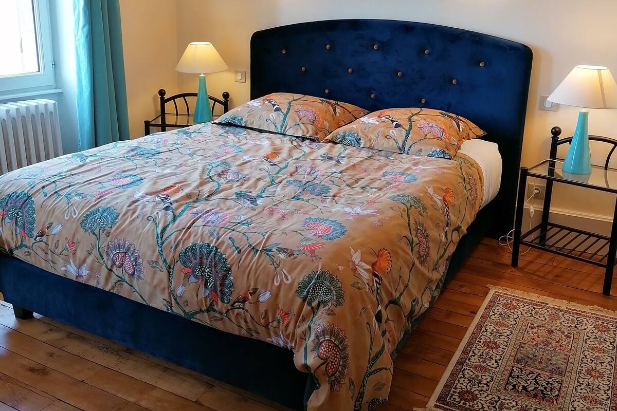 A bedroom with a large bed, two bedside lamps, a radiator, and a patterned rug.