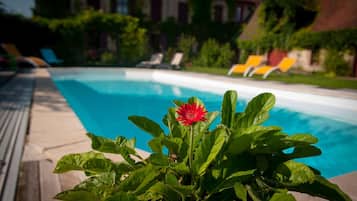 En swimmingpool med en rød blomst i forgrunden, omgivet af grønt og en bygning i baggrunden.