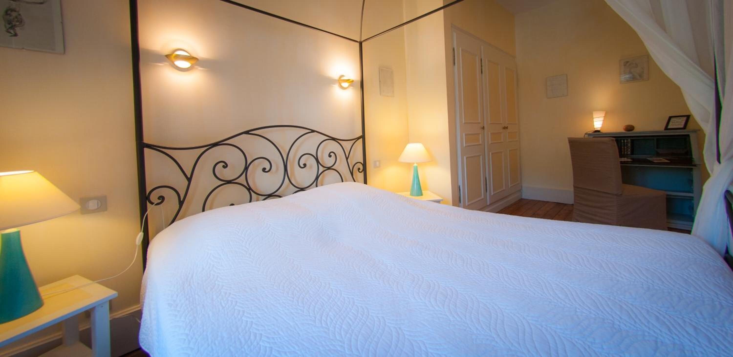 A neatly arranged bedroom with a large bed, bedside lamps, a dresser, and a wardrobe.