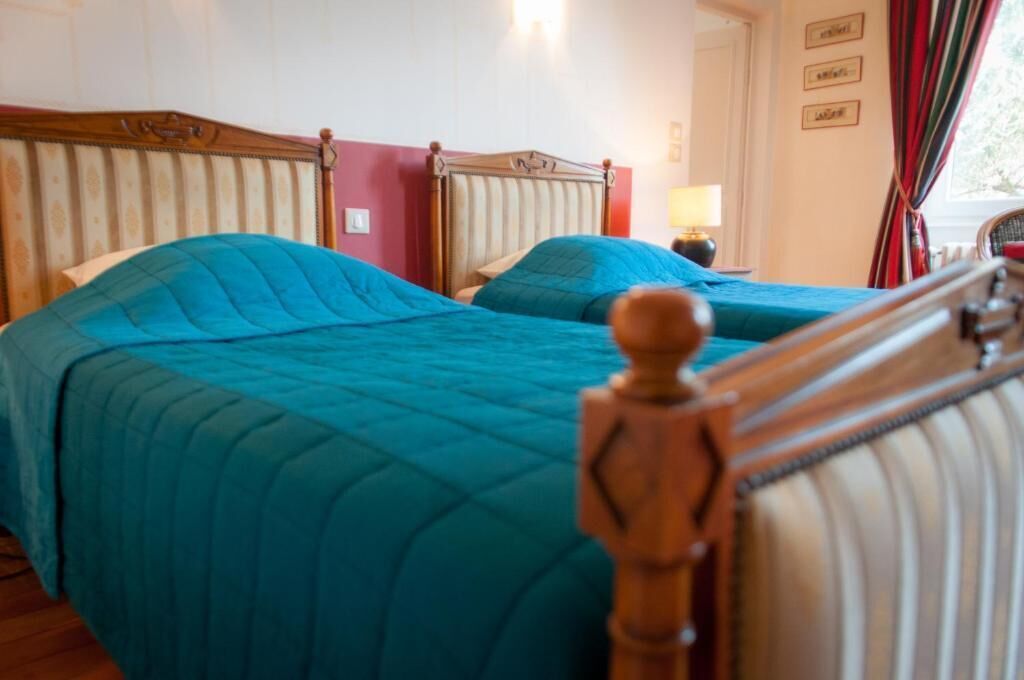 Habitación de hotel con dos camas, cada una con cabecero de madera y ropa de cama azul.