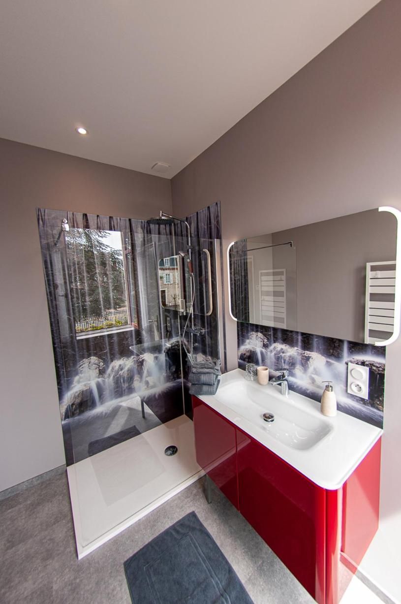 A modern bathroom with a glass shower enclosure, a red vanity, and a large mirror.