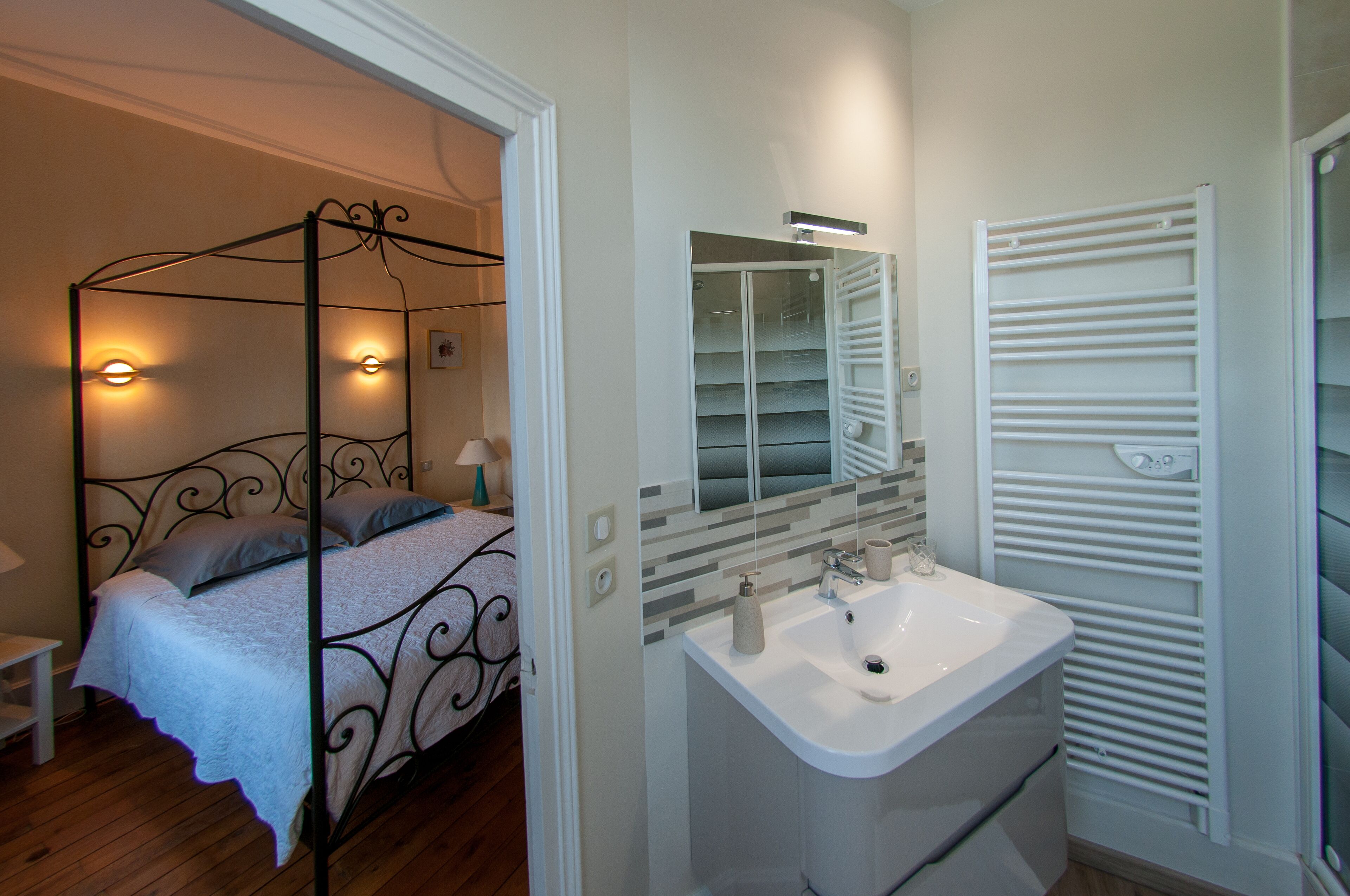 A bedroom with a four-poster bed, a white sink, and a walk-in closet with a mirrored closet rod.