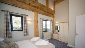 A bedroom with a bed, a dresser, and a wardrobe. There are windows with curtains, a mirror, and a light fixture. - Braisty Woods - Hopes & Beams (Harrogate)